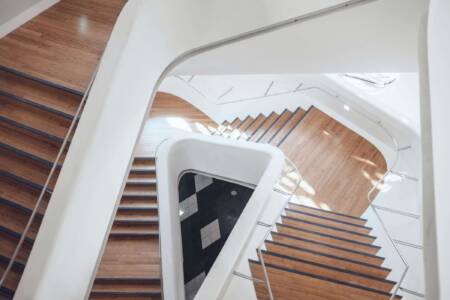 Moderne Holztreppe mit weißem Geländer in einem hellen Treppenhaus