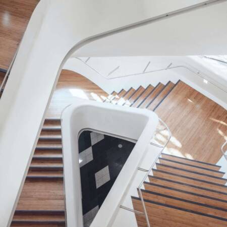 Moderne Holztreppe mit weißem Geländer in einem hellen Treppenhaus